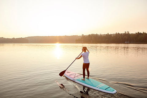 a female paddle boarding at sunset