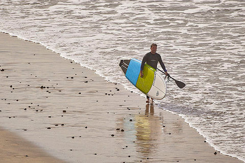 a stand up paddle boarder walking on the beach